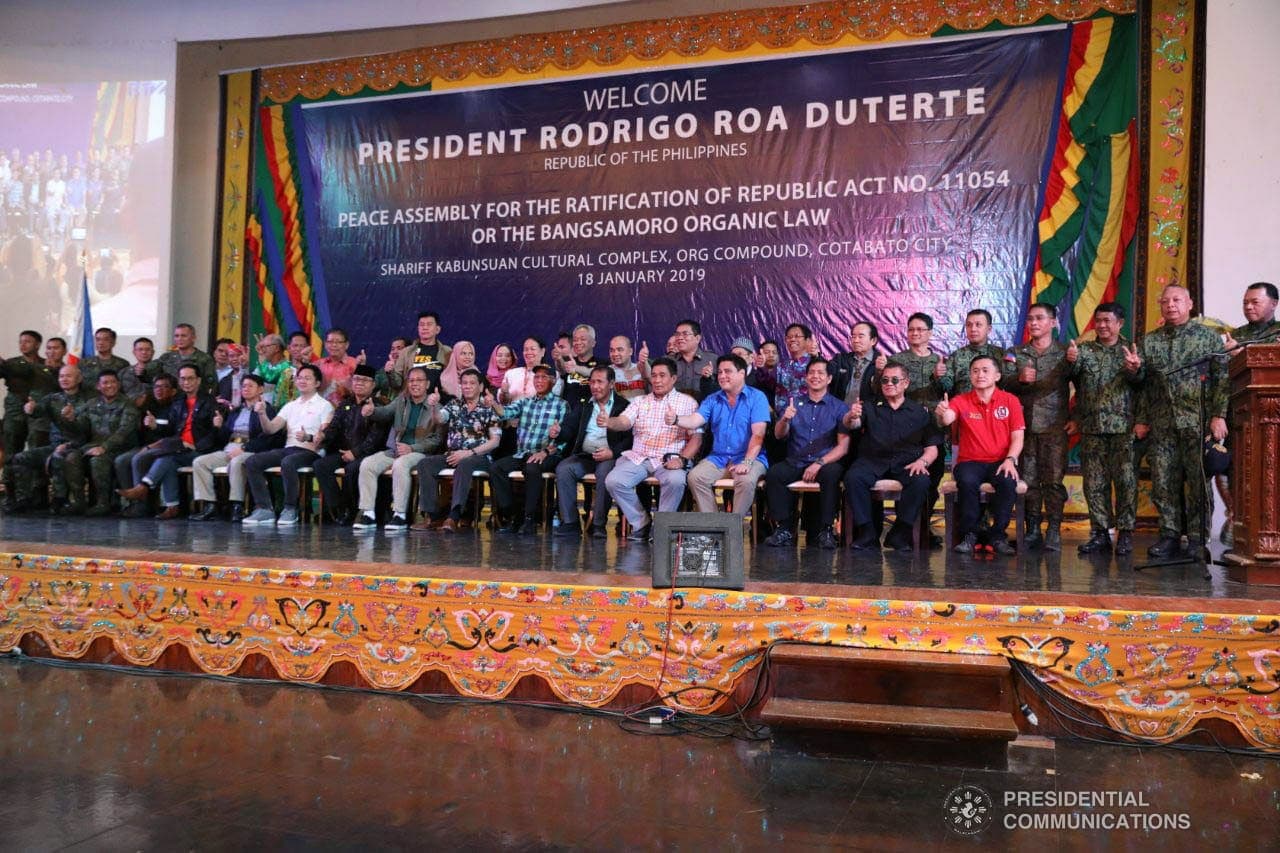 A hall of seated officials beneath a banner reading Peace Assembly for the Ratification of Republic Act No. 11054.