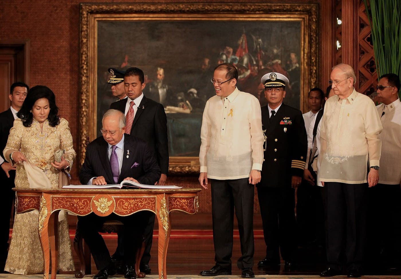 Malaysian Prime Minister Najib Razak signing a book at a table in Malacañan Palace as President Aquino watches.