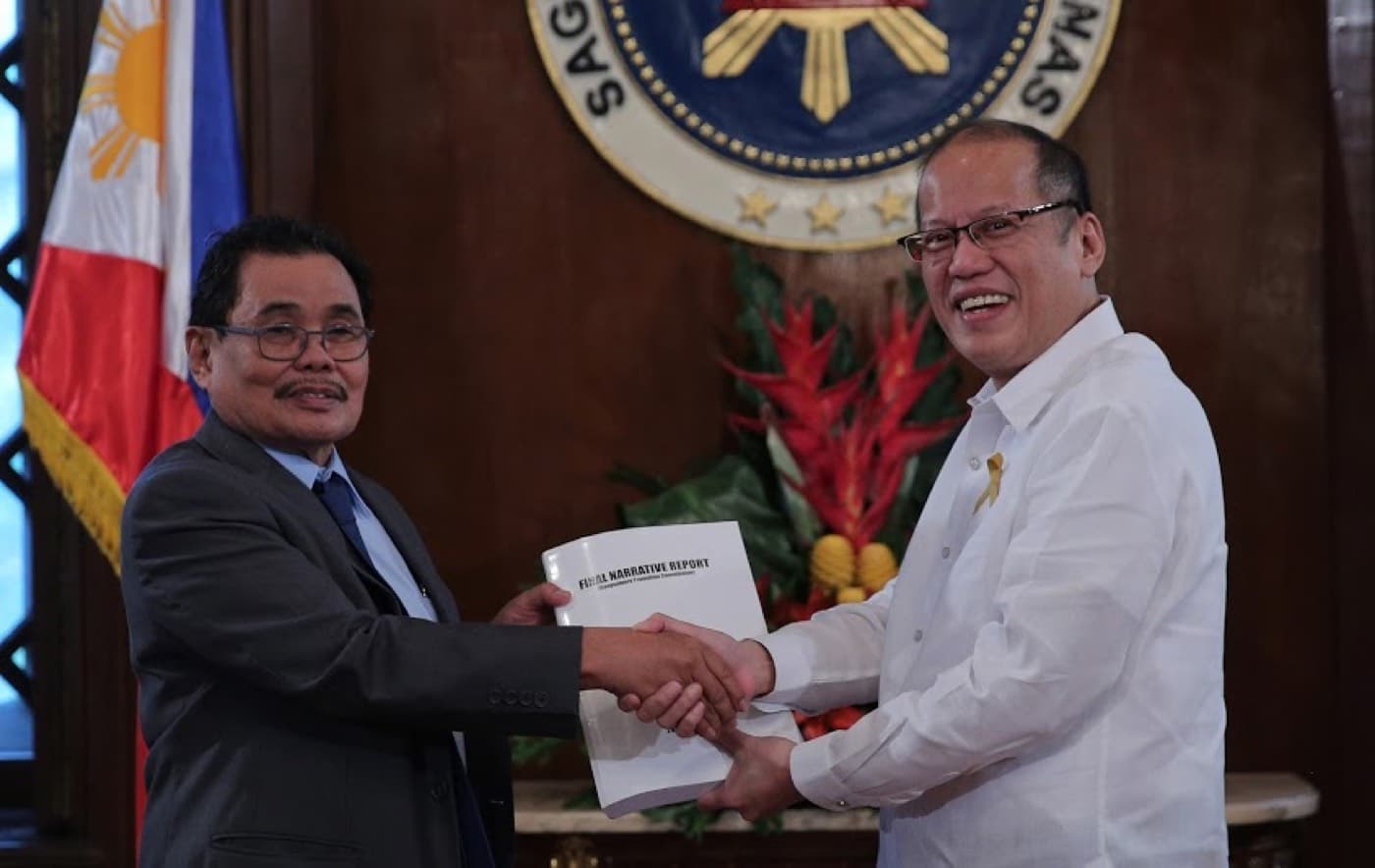 Mohagher Iqbal and President Benigno Aquino III shaking hands over a bound report before the Philippine seal.