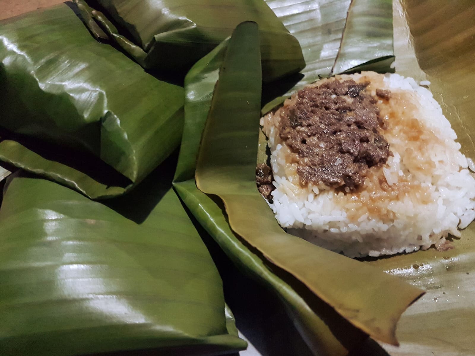 Banana-leaf parcels of pastil, one opened to show shredded meat over steamed rice.