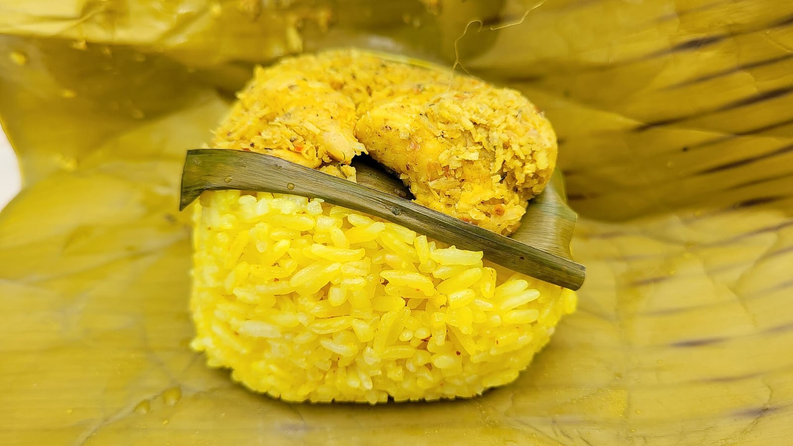 Turmeric-yellow kuning rice and grilled chicken pater served on a banana leaf.
